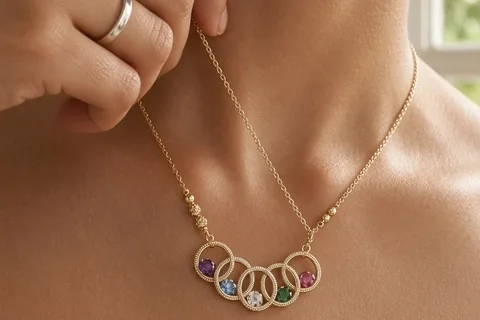 A woman's hand adjusting a gold necklace with five interlocking rings around her neck in a home setting with soft natural lighting