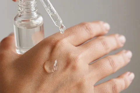 Close-up of a woman's hand applying azelaic acid serum from a dropper bottle to her skin