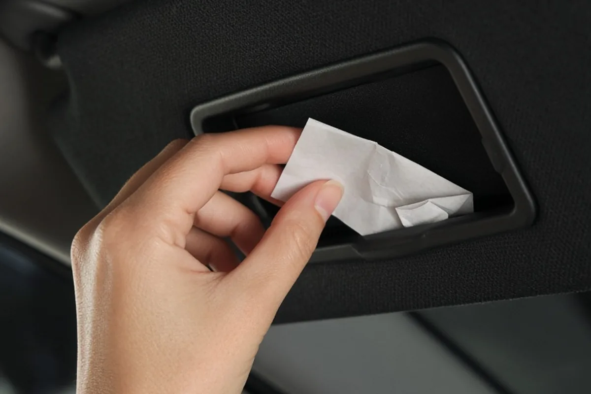 A hand reaching into a car visor and placing a folded note in close-up three-quarter angle view