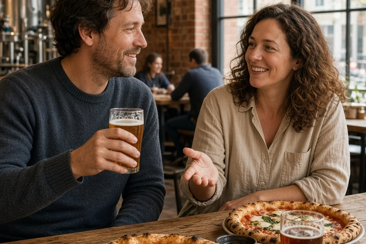 A couple toasting with craft beer and sharing wood-fired pizza at a brewery table