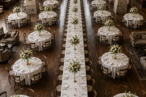 Hybrid wedding reception table layout in historic ballroom with banquet tables between four masonry pillars and round tables around the walls